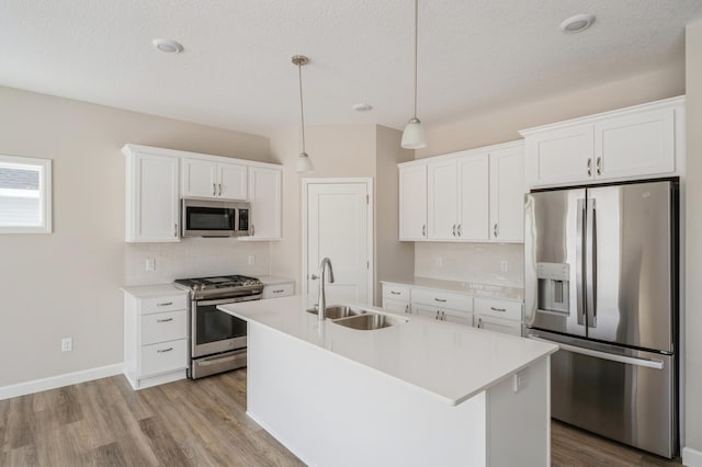 kitchen with sink, white cabinetry, pendant lighting, stainless steel appliances, and a kitchen island with sink