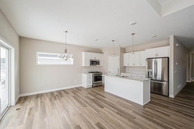 kitchen featuring appliances with stainless steel finishes, decorative light fixtures, white cabinetry, an island with sink, and sink