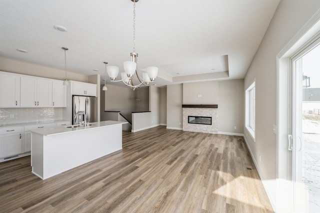 kitchen featuring a kitchen island with sink, decorative light fixtures, white cabinets, and stainless steel refrigerator with ice dispenser