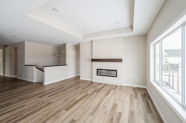 unfurnished living room with a raised ceiling, a stone fireplace, and light wood-type flooring