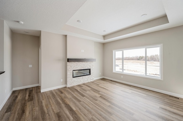 unfurnished living room with wood-type flooring, a fireplace, a raised ceiling, and a textured ceiling