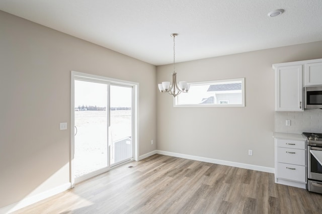 kitchen with appliances with stainless steel finishes, pendant lighting, white cabinets, decorative backsplash, and light wood-type flooring