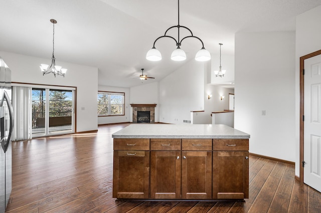 kitchen featuring dark wood-type flooring, a center island, pendant lighting, a fireplace, and ceiling fan with notable chandelier