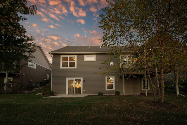 back house at dusk with a lawn and a patio