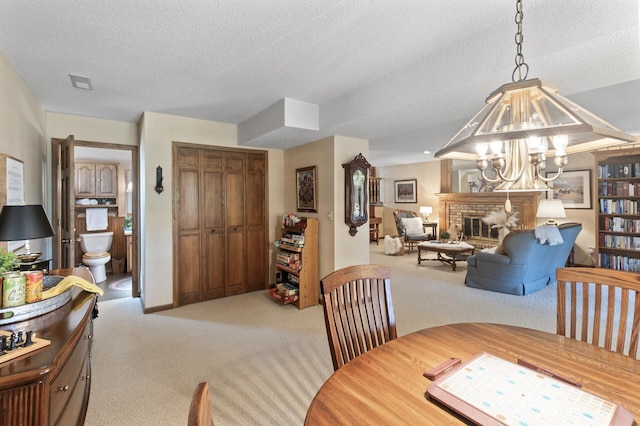 dining room with light colored carpet, a notable chandelier, a brick fireplace, and a textured ceiling