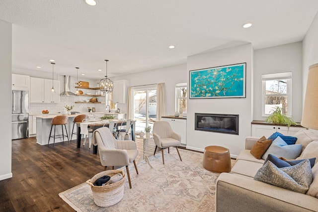 living area featuring a notable chandelier, recessed lighting, dark wood-type flooring, and a glass covered fireplace