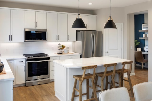 kitchen featuring white cabinetry, a center island, pendant lighting, stainless steel appliances, and backsplash