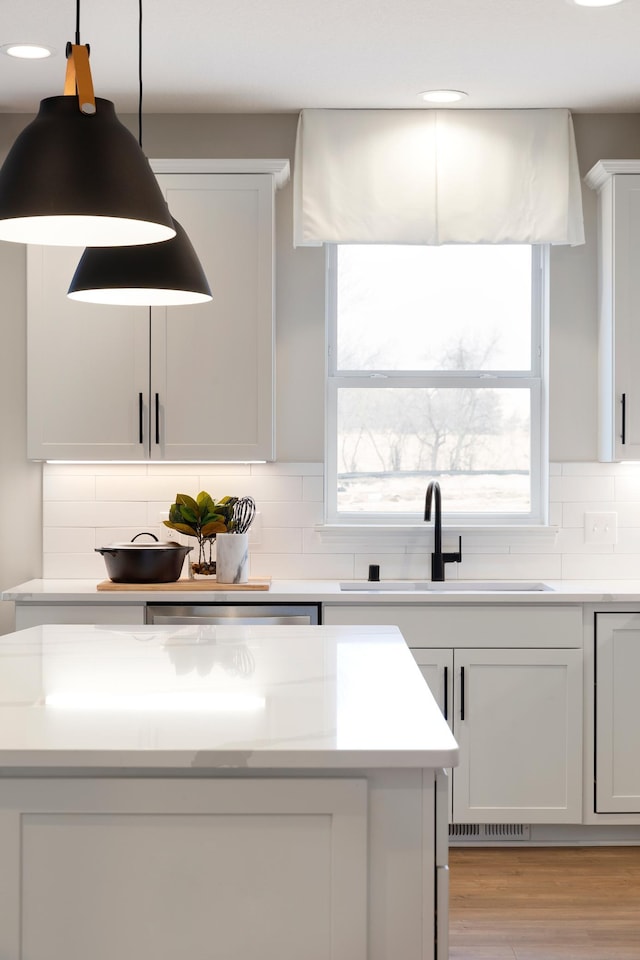 kitchen with sink, hanging light fixtures, light stone countertops, decorative backsplash, and light wood-type flooring