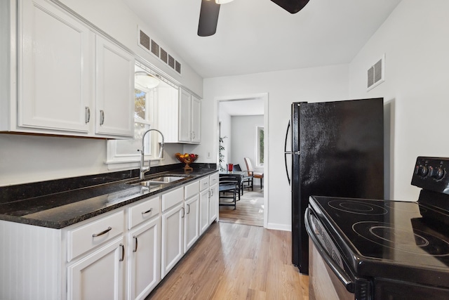 kitchen with black electric range oven, sink, dark stone countertops, light hardwood / wood-style floors, and white cabinets