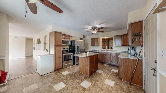 kitchen with sink, a textured ceiling, appliances with stainless steel finishes, a kitchen island, and ceiling fan