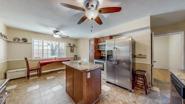 kitchen with ceiling fan, stainless steel appliances, a center island, and a textured ceiling