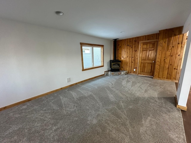 unfurnished living room with wood walls, dark colored carpet, and a wood stove