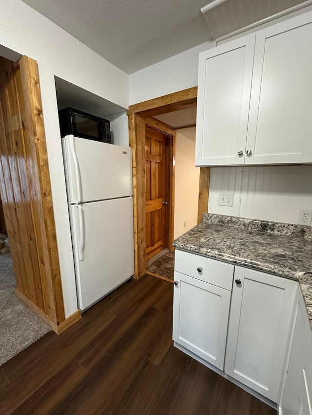 kitchen featuring dark stone countertops, white cabinets, white refrigerator, and dark hardwood / wood-style flooring