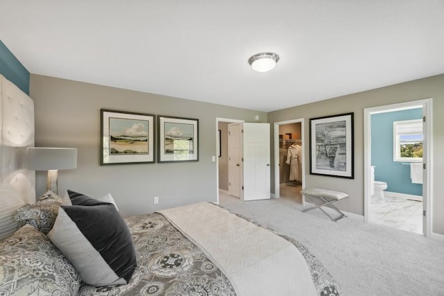 bedroom with a spacious closet, light colored carpet, and ensuite bath