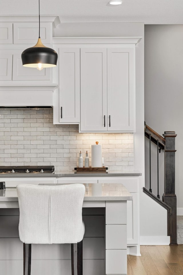 kitchen with light wood-type flooring, pendant lighting, white cabinets, and backsplash