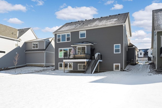 snow covered back of property with a deck and central AC unit