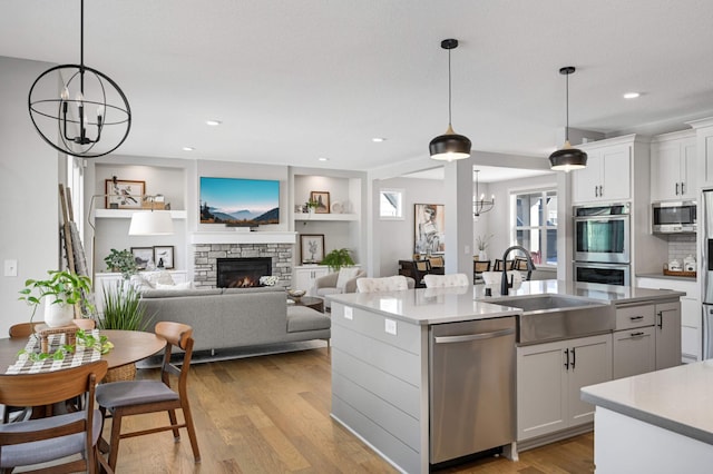 kitchen with sink, appliances with stainless steel finishes, a notable chandelier, a kitchen island with sink, and white cabinets