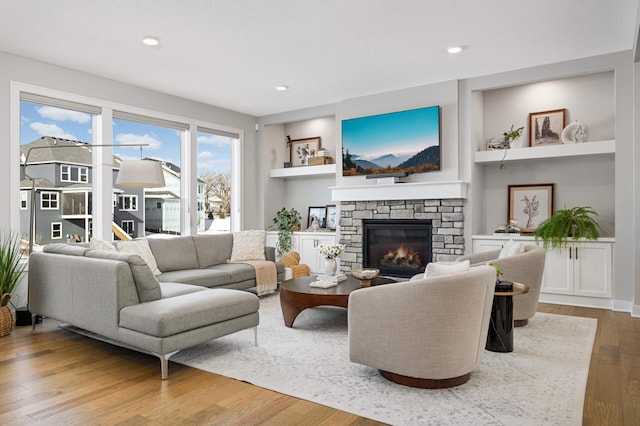 living room featuring built in shelves, a fireplace, and light hardwood / wood-style floors