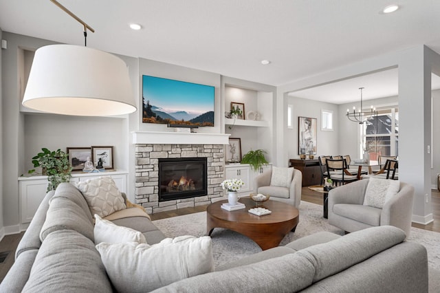 living room with an inviting chandelier, hardwood / wood-style flooring, a stone fireplace, and built in shelves