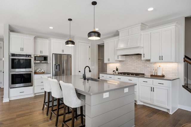 kitchen with sink, hanging light fixtures, an island with sink, stainless steel appliances, and white cabinets