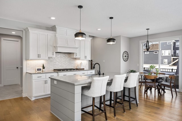 kitchen featuring tasteful backsplash, hanging light fixtures, an island with sink, stainless steel gas stovetop, and white cabinets