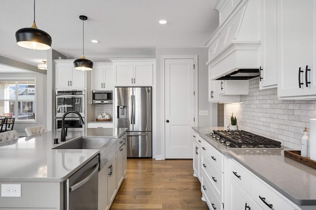 kitchen featuring sink, white cabinetry, stainless steel appliances, a center island with sink, and decorative light fixtures