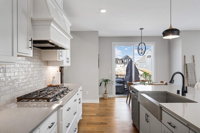 kitchen with sink, custom exhaust hood, white cabinetry, decorative light fixtures, and stainless steel appliances