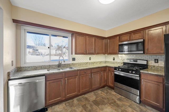 kitchen with light stone counters, stainless steel appliances, sink, and decorative backsplash