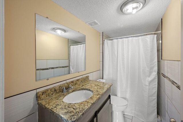 bathroom featuring vanity, tile walls, a textured ceiling, and toilet