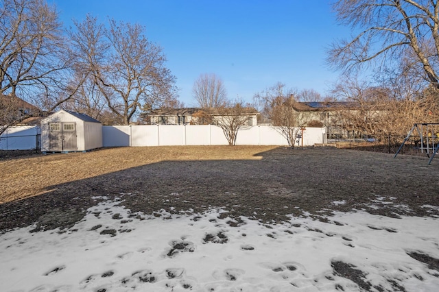 yard covered in snow featuring a playground and a storage unit