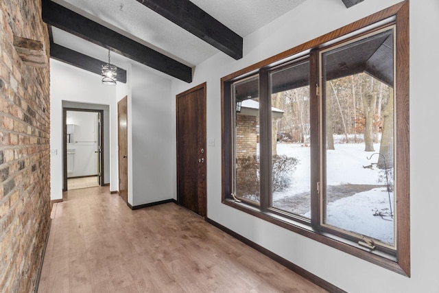 hallway with wood-type flooring, lofted ceiling with beams, a textured ceiling, and a wealth of natural light