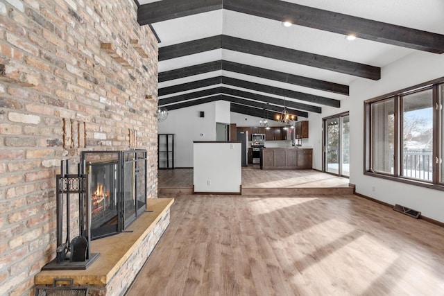 unfurnished living room with lofted ceiling with beams, a brick fireplace, an inviting chandelier, and light wood-type flooring