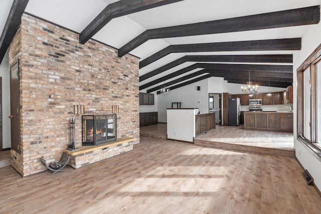 unfurnished living room with vaulted ceiling with beams, sink, a notable chandelier, light hardwood / wood-style floors, and a brick fireplace