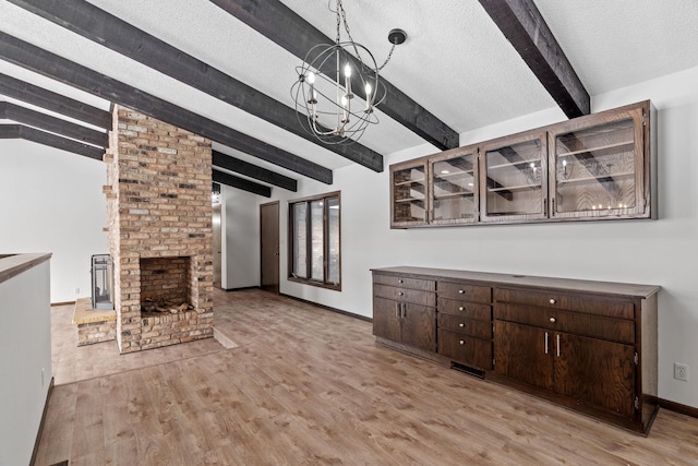 unfurnished living room with an inviting chandelier, lofted ceiling with beams, a textured ceiling, a brick fireplace, and light wood-type flooring