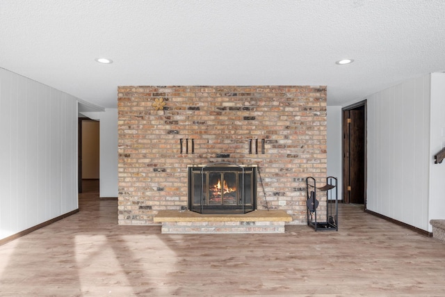 unfurnished living room featuring wood-type flooring, a brick fireplace, and a textured ceiling