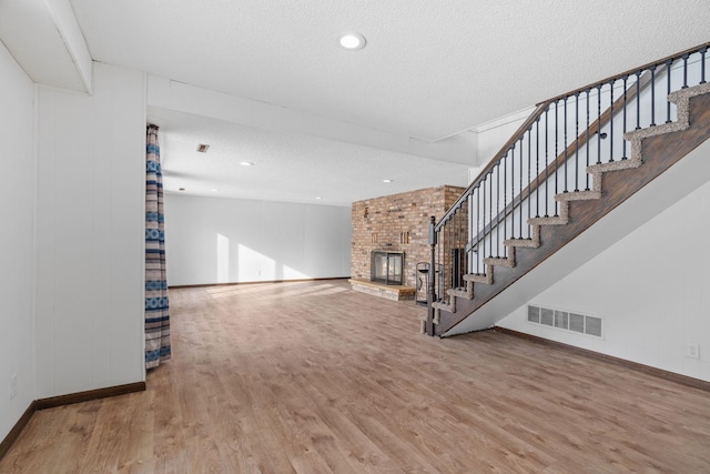 unfurnished living room with hardwood / wood-style floors, a textured ceiling, and a brick fireplace