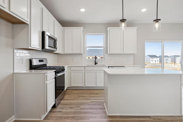 kitchen with sink, stainless steel appliances, light hardwood / wood-style floors, white cabinets, and decorative light fixtures