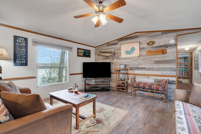 living room featuring wooden walls, ceiling fan, wood finished floors, lofted ceiling, and ornamental molding