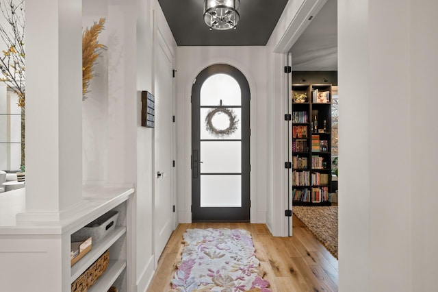 foyer with light wood-style flooring, arched walkways, and a notable chandelier