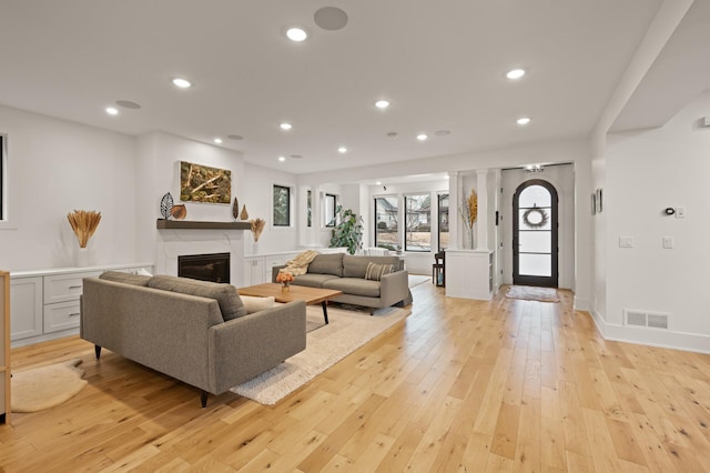 living room featuring recessed lighting, visible vents, baseboards, light wood-style floors, and a glass covered fireplace