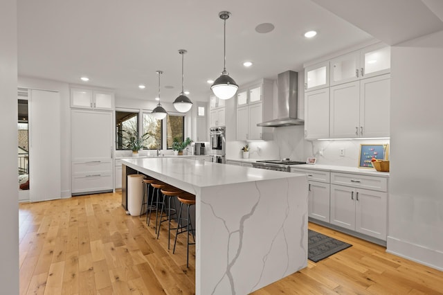 kitchen with a kitchen breakfast bar, light wood-style floors, white cabinets, wall chimney range hood, and a center island