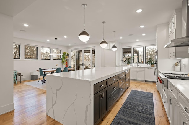 kitchen featuring recessed lighting, wall chimney range hood, light wood-style flooring, and a center island