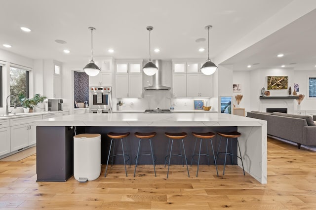 kitchen featuring light wood finished floors, decorative backsplash, white cabinets, wall chimney range hood, and a sink