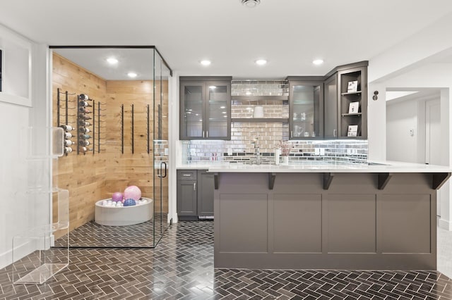 interior space featuring a breakfast bar area, gray cabinetry, light countertops, backsplash, and open shelves