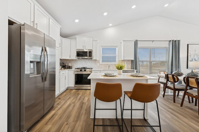 kitchen featuring backsplash, stainless steel appliances, white cabinets, vaulted ceiling, and light wood-type flooring