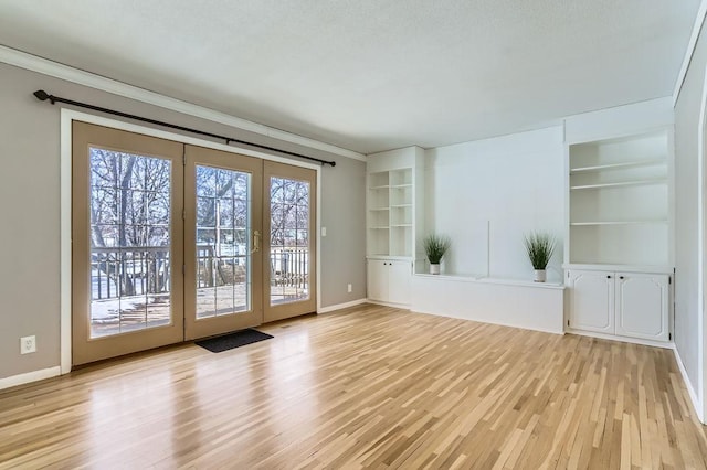 unfurnished living room with crown molding, light wood-style flooring, built in features, and baseboards