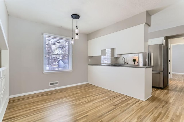 kitchen featuring a peninsula, light wood-style flooring, freestanding refrigerator, white cabinetry, and backsplash