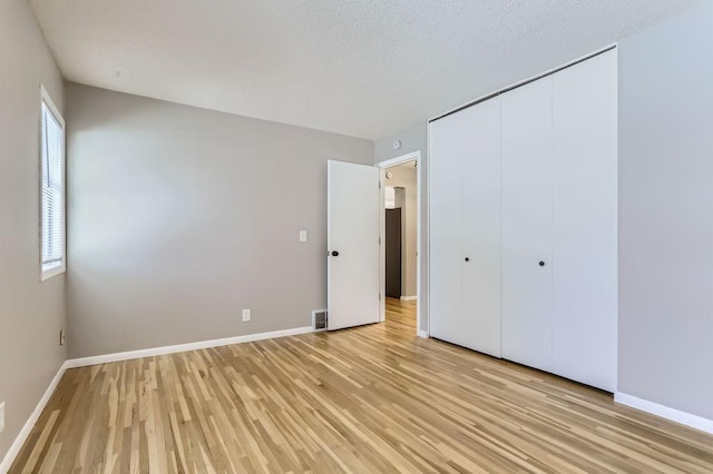 unfurnished bedroom featuring a closet, light wood-style flooring, a textured ceiling, and baseboards