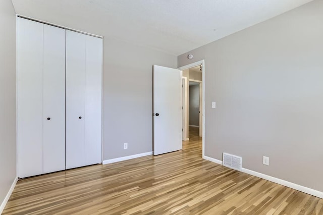 unfurnished bedroom featuring a closet, visible vents, light wood-style flooring, and baseboards