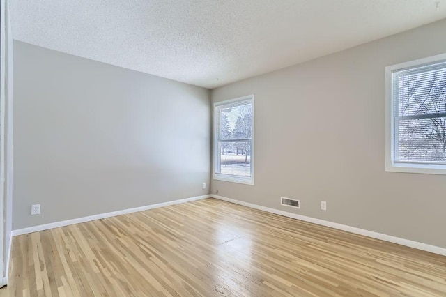 empty room with light wood-type flooring, visible vents, baseboards, and a textured ceiling